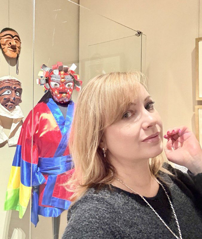 Посетительница на фоне витрины с масками и костюмами в Музее Востока — фотография в экспозиционном пространстве без указания имени.