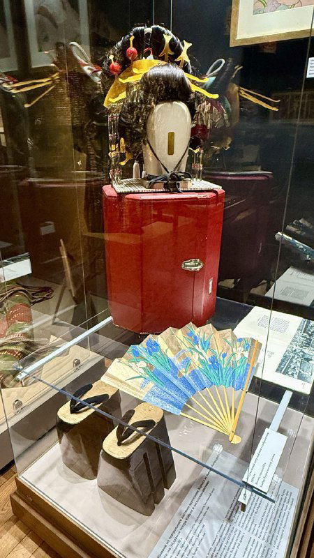 Витрина с театральными аксессуарами: веер, сандалии и причёска-головной убор — элементы сценического реквизита на выставке.