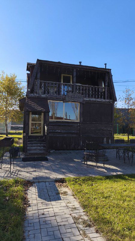 Двухэтажное деревянное строение и прилегающая дорожка на территории базы отдыха, тёплая атмосфера загородного комплекса.