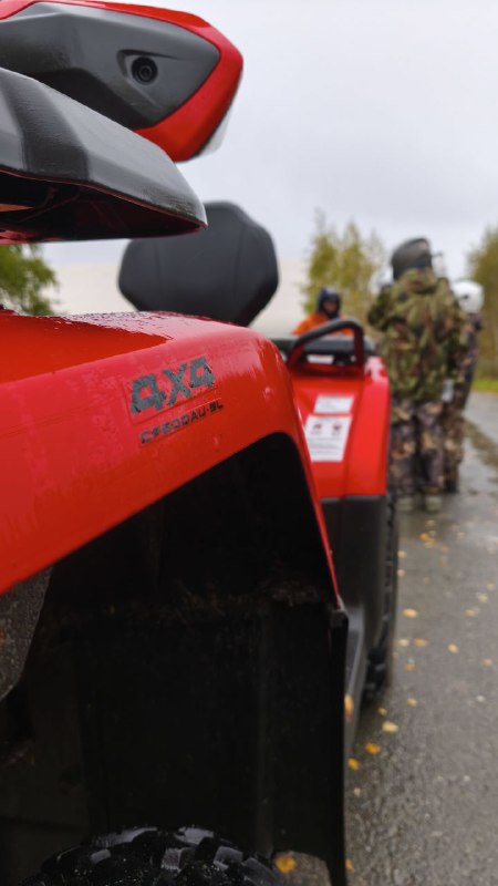 Детальный кадр красного квадроцикла в строю; видно маркировку на пластике и участников, готовящихся к старту в колонне машин.