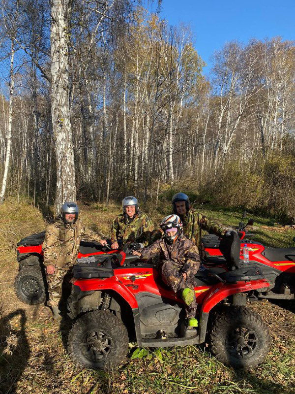 Трое людей на квадроциклах на лесной тропе среди высоких берёз, осенняя атмосфера и ровная дорога, участники в шлемах и камуфляже.