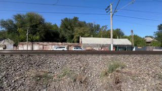 Берег у набережной Аксай: железнодорожные рельсы на переднем плане, строения и деревья за ними при ясной дневной погоде.