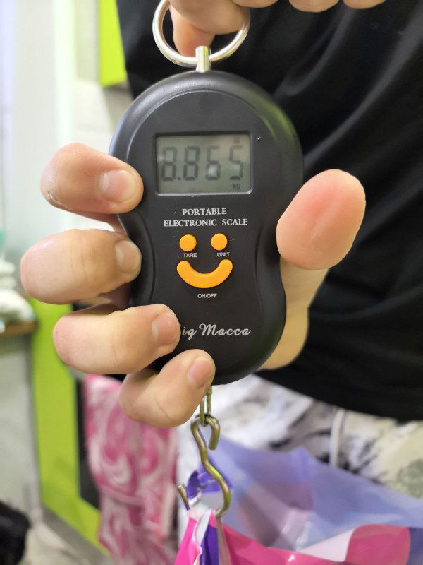 Ручные электронные весы в руках, крупный план на дисплей с показанием примерно 8.65 кг; процесс взвешивания крупной партии рыбы.