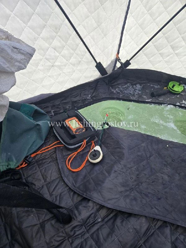 Внутренний вид палатки с эхолотом и моталкой рядом с лункой — техника и снасти для эффективной зимней рыбалки на реке.