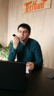 Мужчина в клетчатой рубашке делает холодный звонок за рабочим столом с ноутбуком, держит смартфон у рта в офисе.