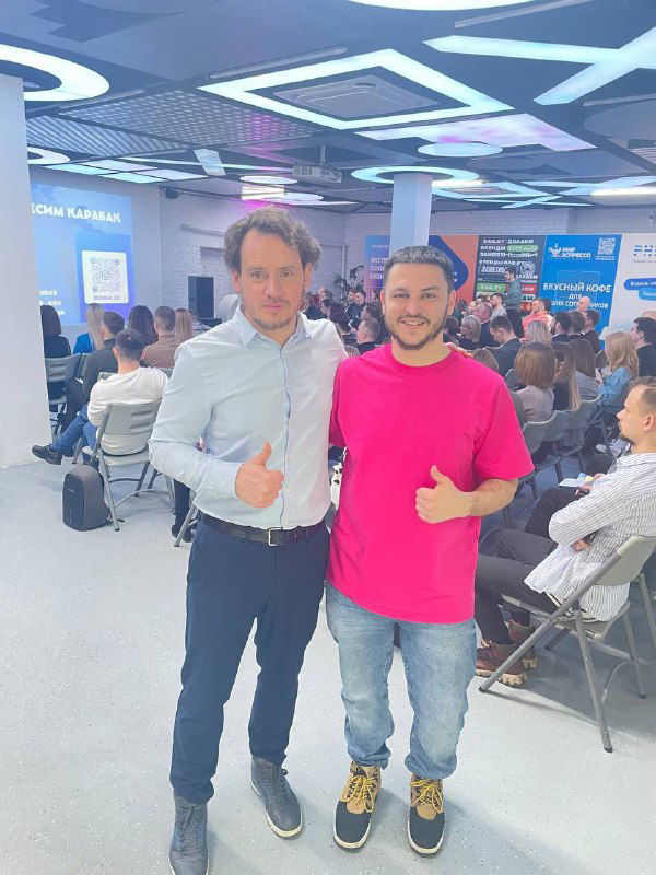 Фото автора вместе с Андреем Карпенко на фоне конференции: двое стоят на переднем плане, за ними видна аудитория и экран события.