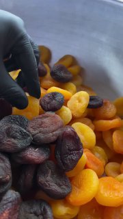 Миска с тёмными и оранжевыми сухофруктами (чернослив и курага), рука в перчатке берёт плод — фото к совету о сухофруктах.