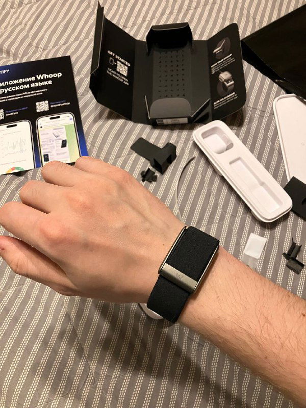 Whoop 5.0 на запястье автора во время распаковки: браслет на руке, рядом видны комплектующие и открытая упаковка.
