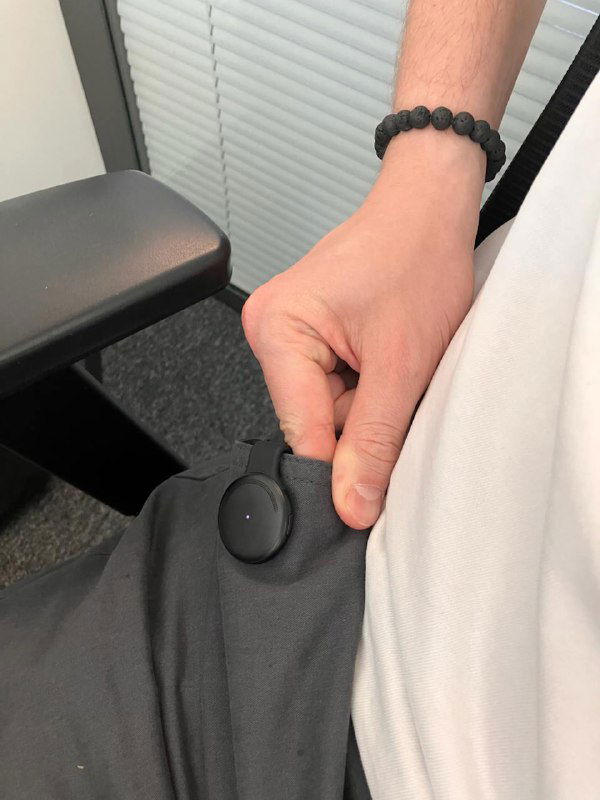 Крупный план: человек крепит Limitless Pendant на одежду у пояса, показан способ фиксации магнитами и резинкой, съёмка в офисной обстановке.