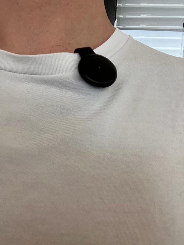 Pendant на шее: крупный план аксессуара на белой футболке человека, видна верёвочная подвеска и компактный круглый корпус устройства.