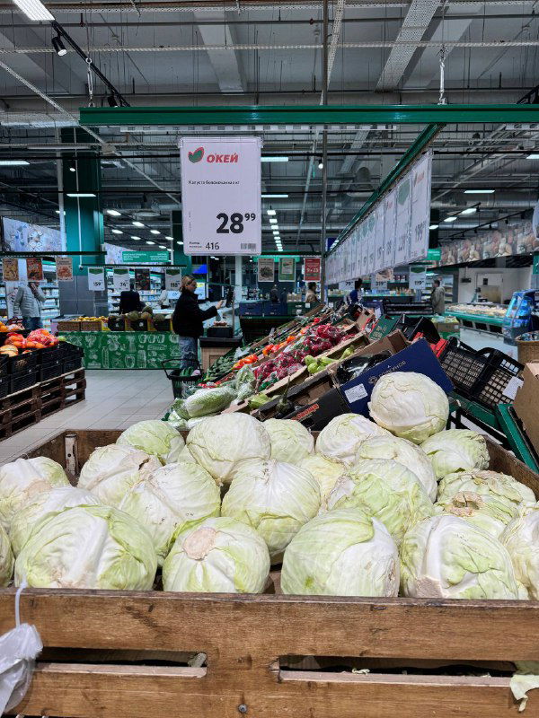 Ряд белокочанной капусты на деревянных поддонах с крупным ценником 28₽ за кг, торговая зона с продукцией осеннего сезона.