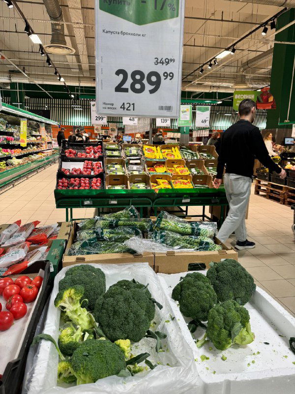 Разложенные головки брокколи в лотках у ценника 289₽ кг, общий вид отдела овощей и дальние полки с продукцией.
