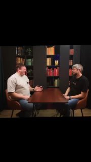 Двое мужчин сидят за столом в студии-интервью, полки с книгами на заднем плане — кадр из ролика об экономии электричества в Германии.