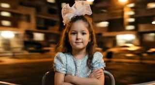 Кинематографичный ночной портрет ребёнка на низкой металлической дворовой карусели: ребёнок по пояс в центре кадра, руки скрещены, фон сильного motion blur.