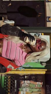 Крупный план: модель в солнечных очках и светлом парике держит стакан напитка на фоне уличной витрины и граффити, акцент на аксессуарах.