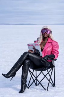 Модель в ярко-розовой куртке и кожаных ботфортах сидит на складном кресле на снегу, читает глянец, стиль fashion editorial.