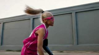 Боковой профиль игрока в спортивной экипировке на фоне серой стены, волосы развеваются, видна фокусировка движения и рабочая среда площадки.