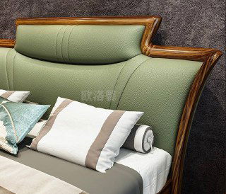 Крупный кадр изголовья кровати с плавной формой и мягкой кожаной обивкой зелёного оттенка; видны швы, текстура кожи и древесный кант.