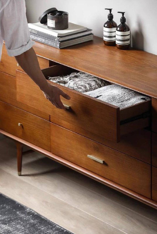 Рука открывает выдвижной ящик комода, показывая вместимость и аккуратную внутреннюю отделку, практический кадр использования мебели.