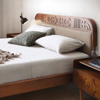 Крупный план изголовья кровати Madrid: резной деревянный декор, обивка в мягкой текстуре, декоративная подушка и настенный светильник.