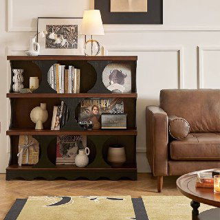 Компактная вариант книжной полки из массива ясеня в насыщенном тёмном оттенке, на полках книги и керамика, рядом кожаный диван в образе гостиной.