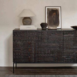 Тёмный резной комод из массива ясеня в интерьерной постановке: настольная лампа, картина и декоративные предметы, вид сбоку.