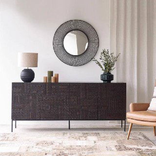 Комод из ясеня в гостиной постановке, тёмный резной фасад, зеркало и кресло рядом, стильная декоративная компоновка.