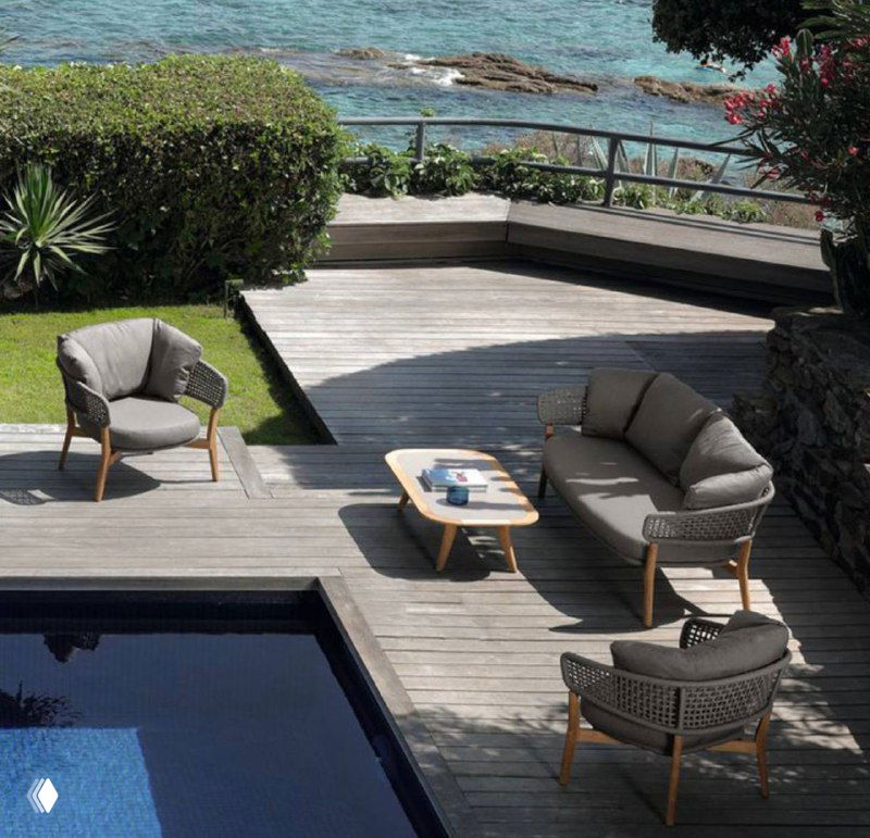 Комплект уличной мебели на деревянном настиле у бассейна: кресла и кофейный столик в серых тонах, ротанг и дерево.