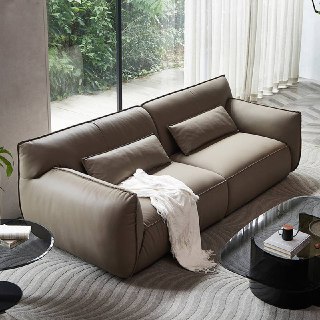 Диван Navola в кожаной обивке, ракурс слева сверху, две декоративные подушки и плед, интерьер с зеленью за окном