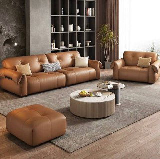 Широкий кожаный диван с креслом и оттоманкой в светлой гостиной: общий ракурс показывает комплект мебели и декоративные элементы на полках.