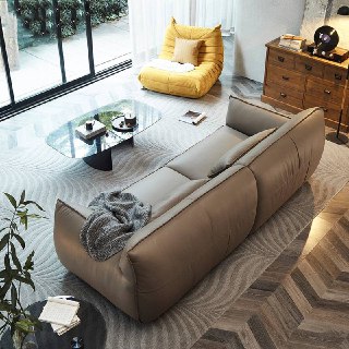 Вид сзади и с угла дивана Navola в кожаной отделке, интерьер с деревянным полом и креслом в фоне