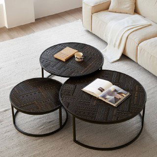 Три круглых журнальных столика тёмного цвета с рельефной поверхностью, на одном лежит книга и стоит кружка, фон — светлый диван.