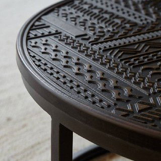 Крупный план резного узора на тёмной столешнице журнального столика и часть металлической ножки — текстура и финиш покрытия.