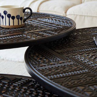 Фрагмент верхней поверхности двух соединённых столиков с чашкой на переднем плане — отделка и рисунок столешницы видны вблизи.