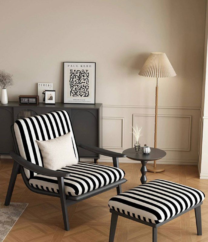 Кресло из ясеня с полосатой обивкой и пуфом в светлой комнате: вид под углом на сиденье и деревянные ножки, декоративные элементы вокруг.