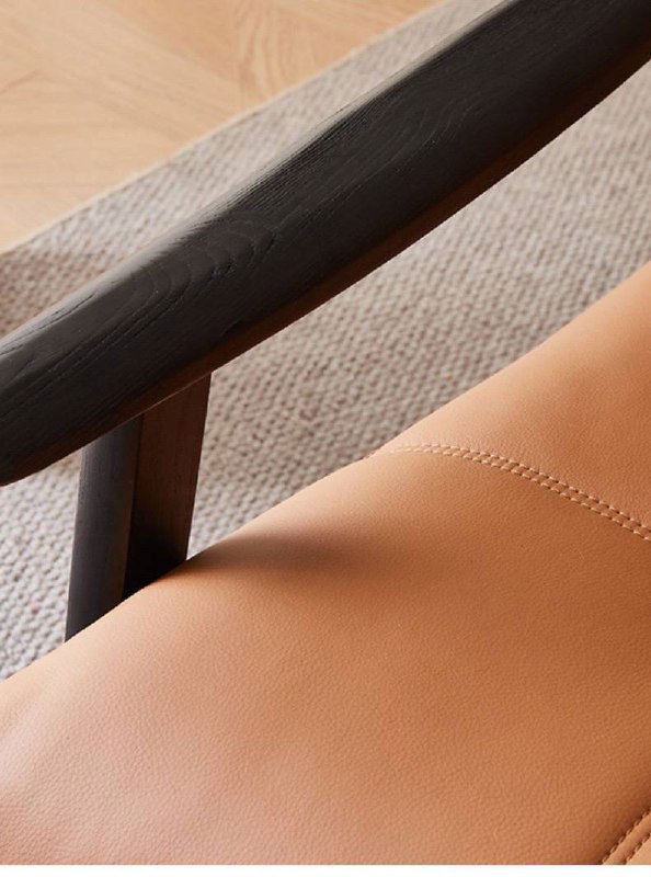 Деталь деревянного подлокотника и части сиденья кресла из ясеня: тёмный массив дерева, ровная поверхность и соприкосновение с кожей.