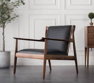 Кресло из массива ясеня с кожаной сидушкой и спинкой, крупный план под углом, окружение интерьерного стиля и декоративные растения.