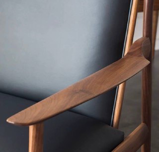 Крупный план подлокотника кресла из массива ясеня с плавной формой и отделкой, чёрная кожаная обивка видна на заднем плане.