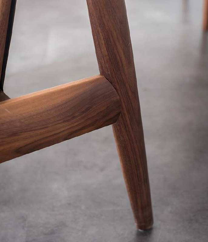 Крупный план ножки и нижней рамы кресла из ясеня, подчёркнуты пропорции, крепления и отделка древесины в натуральном освещении.