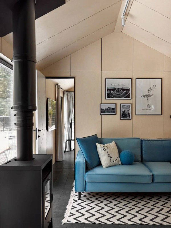 Интерьер с печью-камином и ярким диваном: минималистичная отделка, высокие потолки и вид на лес через окно, тёплая гостиная зона.