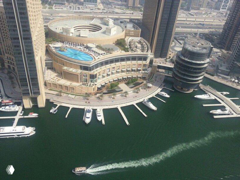 Аэрофотоснимок пристани и прилегающего здания Marina Mall у водной набережной с пришвартованными яхтами и прогулочными катерами.