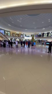 Внутренний вид круглого атриума торгового центра с панорамным обзором магазинов на двух уровнях и проходящими посетителями.