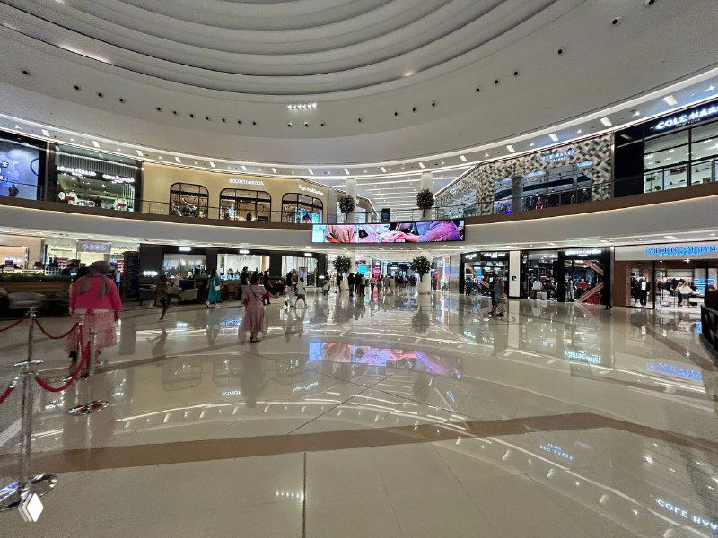 Широкий панорамный вид центральной торговой площади с несколькими уровнями магазинов и открытыми балконами над фудкортом.