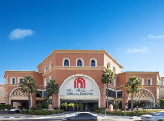 Фасад Mall of the Emirates в классическом архитектурном стиле с арочными галереями, пальмами у входа и вывеской крупного торгового центра.