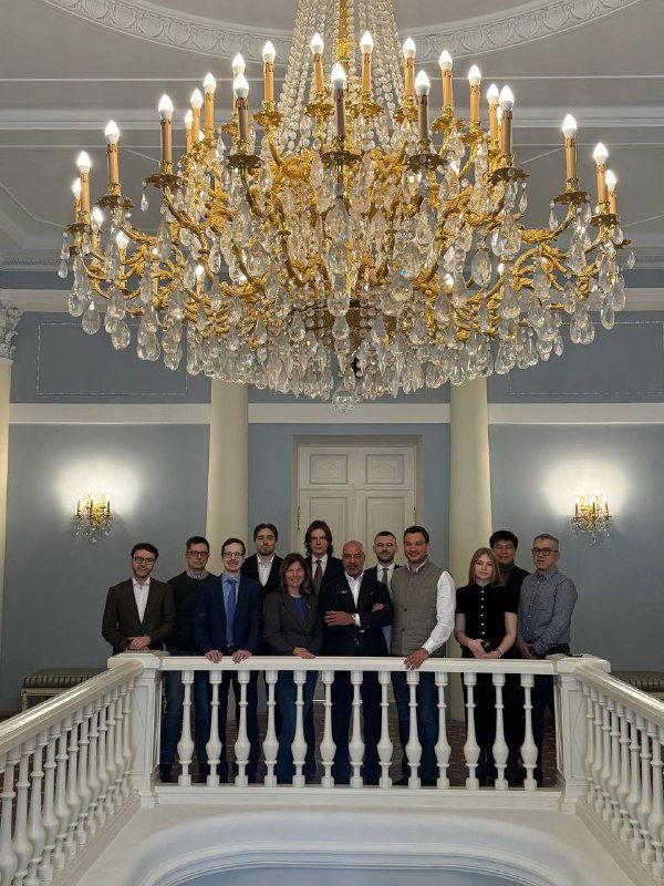 Групповое фото участников на балюстраде под крупной люстрой в помещении UCL: команда экспертов и гости встречи по связям РФ–ОАЭ.