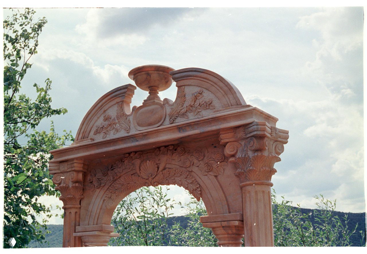 Скан плёнки Kodak Vision3 250D: резная каменная арка на фоне облачного неба, естественные пастельные тона и мелкая зернистость.