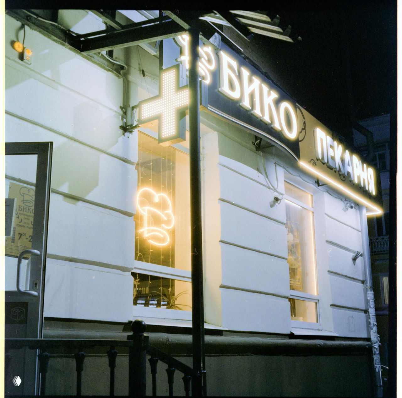 Ночная съёмка фасада пекарни и аптечного креста на плёнке Harman Phoenix II: крест выглядит почти белым, красного цвета на кадре нет.