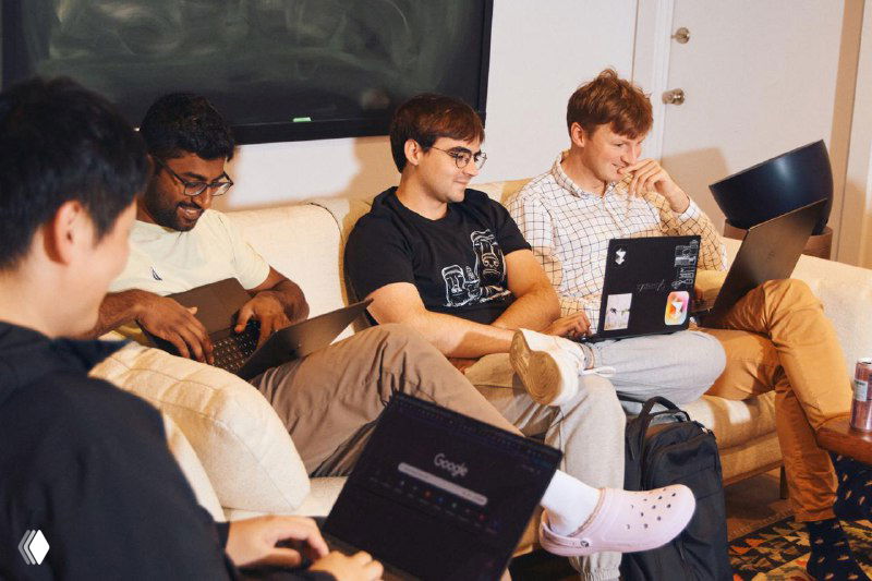 Неформальная зона отдыха Cursor: несколько инженеров на диване с ноутбуками, обсуждающие код и проекты в расслабленной обстановке.