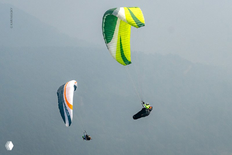 Три параплана на фоне туманных гор; групповой полёт в равнине предгорий Гималаев, лёгкая дымка и масштаб перевалов.