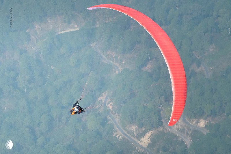 Красный параплан над извилистым горным ландшафтом; вид сверху на глубокие склоны и тропы в долине Гималаев.
